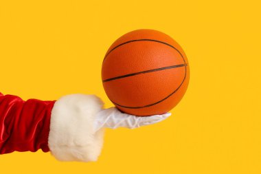 Sarı arka planda basketbol oynamak için topu tutan Noel Baba, yakın plan.