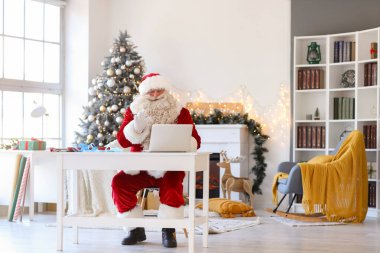 Noel Baba evde dizüstü bilgisayar kullanıyor.