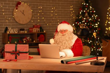 Noel Baba evde dizüstü bilgisayar kullanıyor.