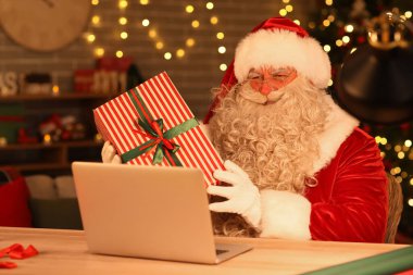 Evde dizüstü bilgisayarı ve Noel hediyesi olan Noel Baba.