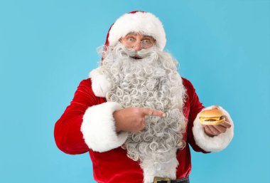 Noel Baba mavi arka planda lezzetli bir burgeri işaret ediyor