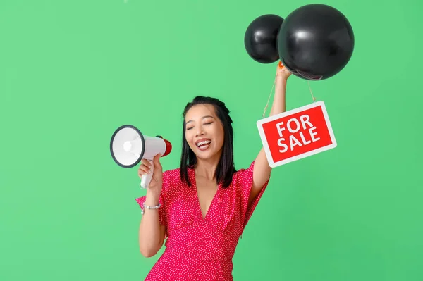 Asian woman with megaphone, balloons and FOR SALE sign on green background