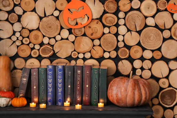 Mantelpiece with books, Halloween pumpkins and burning candles near wooden wall