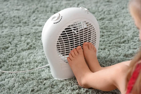 Barefoot little girl warming near electric fan heater in bedroom, closeup