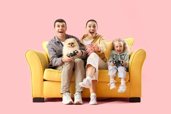 Happy family playing video game on sofa against pink background