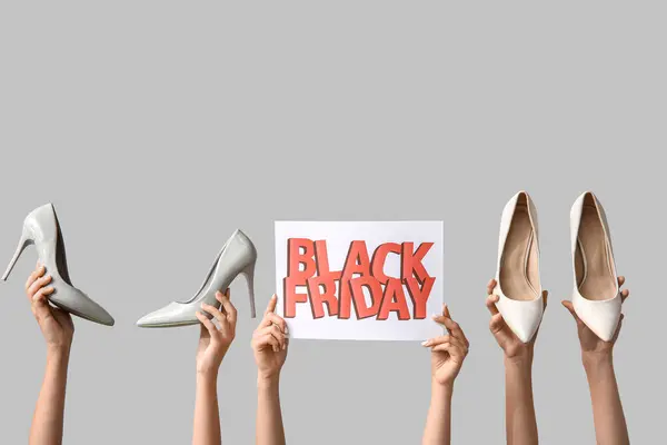 Female hands holding poster with text BLACK FRIDAY and shoes on pink background