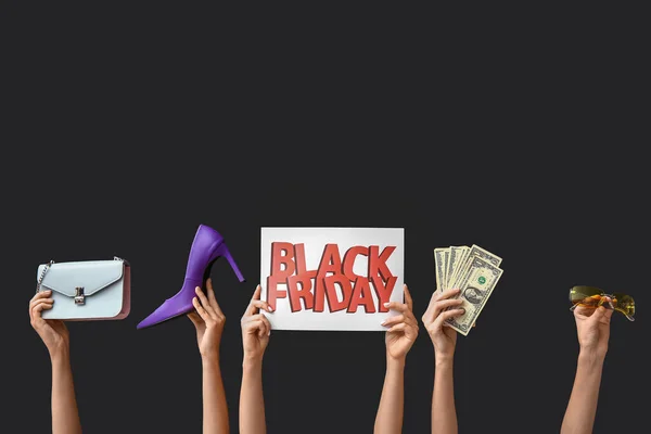 Female hands holding poster with text BLACK FRIDAY, money and women accessories on dark background