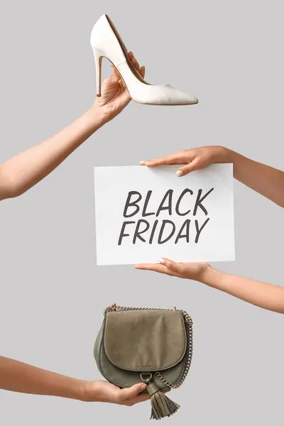 Female hands holding poster with text BLACK FRIDAY and women accessories on grey background