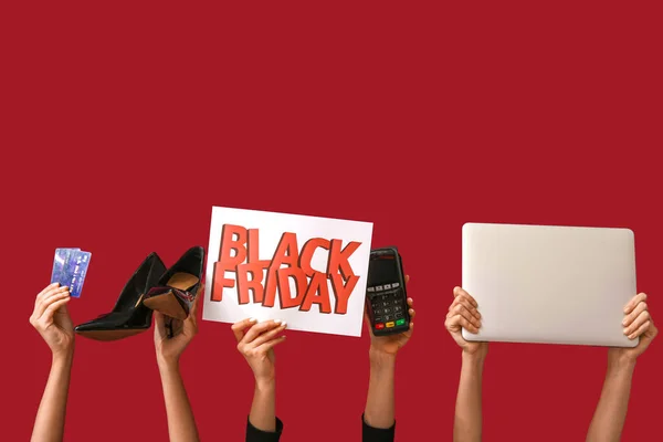 Female hands holding poster with text BLACK FRIDAY, shoes, credit cards, laptop and payment terminal on red background