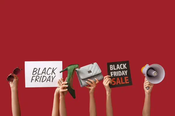 Female hands holding poster with text BLACK FRIDAY, women accessories and megaphone on red background