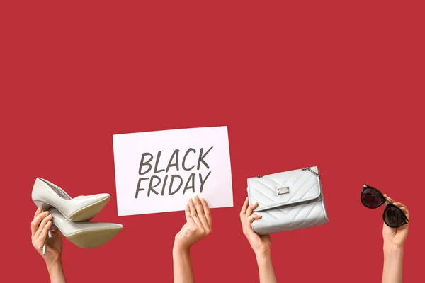 Female hands holding poster with text BLACK FRIDAY and women accessories on red background