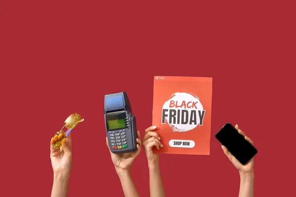 Female hands holding poster with text BLACK FRIDAY, sunglasses, payment terminal and mobile phone on red background