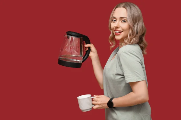 Schöne Junge Frau Mit Modernem Wasserkocher Und Tasse Auf Rotem — Stockfoto