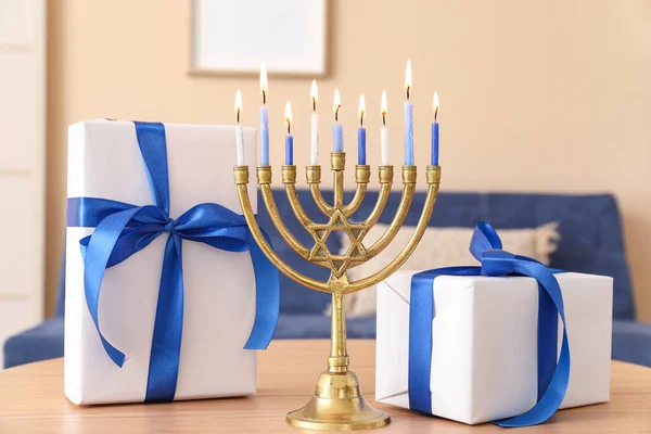 Menorah with burning candles and gift boxes on wooden coffee table in living room, closeup. Hanukkah celebration