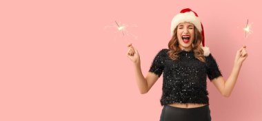 Noel Baba şapkalı ve pembe arka planda Noel fişekleri olan mutlu genç bir kadın.