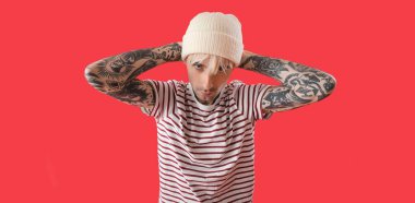 Kırmızı arka planda havalı dövmeli genç bir adam. 