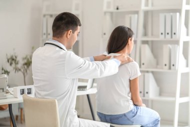 Erkek doktor klinikteki genç kadının duruşunu kontrol ediyor.