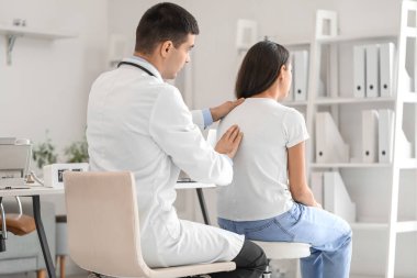Erkek doktor klinikteki genç kadının duruşunu kontrol ediyor.
