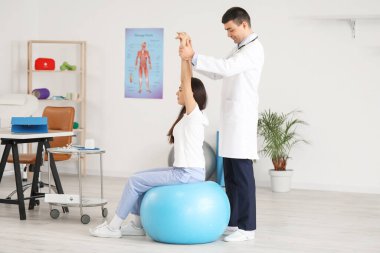 Erkek doktor klinikteki genç kadının duruşunu kontrol ediyor.