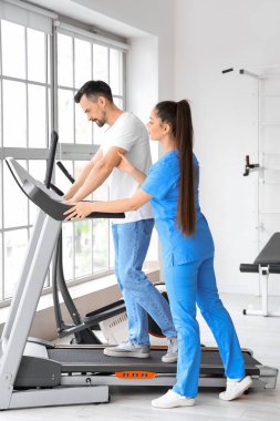 Rehabilitasyon merkezinde koşu bandında genç bir adamla çalışan kadın fizyoterapist.