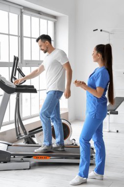 Rehabilitasyon merkezinde koşu bandında genç bir adamla çalışan kadın fizyoterapist.