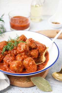 Bir kase domates soslu lezzetli köfte ve beyaz arka planda dereotu.