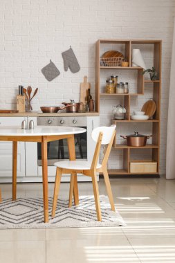 Beyaz tezgahlı, raflı ve yemek masalı bir mutfak.