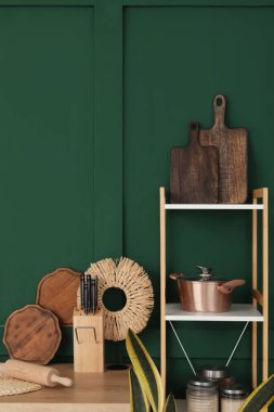Mutfak tezgahı ve yeşil duvarın yanında mutfak aletleri olan raf ünitesi.
