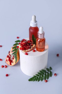 Temel yağ şişeleri, sıva podyum ve hafif arkaplanda nar kompozisyonu