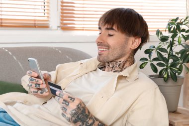 Evde cep telefonu kullanan dövmeli genç bir adam.
