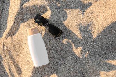 Bir şişe güneş kremi ve kumsalda güneş gözlüğü.