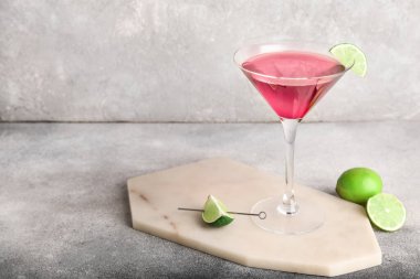 Üzerinde bir bardak Cosmopolitan kokteyli ve gri arka planda limon olan tahta.