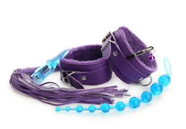 Beyaz arka planda seks dükkanından kırbaç ve anal fiş takılı mor kelepçeler.