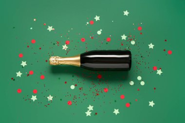 Yeşil arka planda konfeti olan şampanya şişesi.