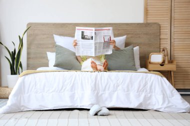 Evdeki yatak odasında gazete okuyan güzel genç bir kadın.