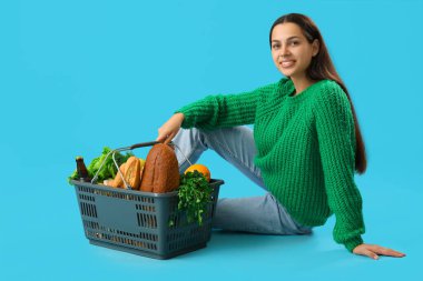 Mavi arka planda alışveriş sepeti olan genç bir kadın.