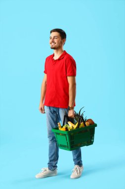 Mavi arka planda alışveriş sepeti olan genç adam.