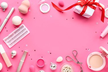 Farklı makyaj ürünlerinden yapılmış çerçeve ve pembe arka planda Noel dekoru