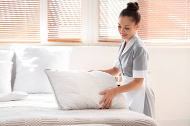 Otel odasında yatak yapan güzel oda hizmetçisi.