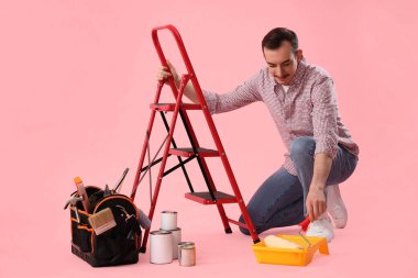 Pembe arka planda merdiven ve inşaat aletleri olan genç bir adam.