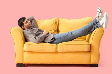 Pembe arka planda sarı koltukta uyuyan yakışıklı genç adam.