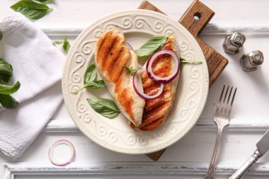 Lezzetli ızgara tavuk göğsü, beyaz arka planda fesleğen ve kırmızı soğan.