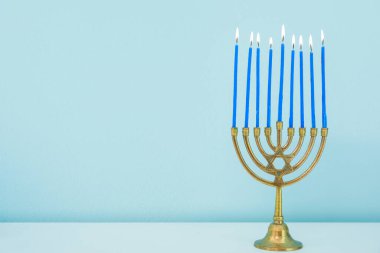 Mavi duvarın yanındaki beyaz masada yanan mumlarla Menorah, yaklaş. Hanuka kutlaması