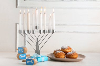 Menorah yanan mumlar, dreidels, hediye ve çörekler ışık masasında Hanuka kutlaması için.