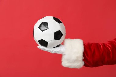 Kırmızı arka planda futbol topuyla Noel Baba eli, yakın plan.