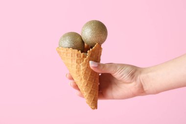 Pembe arka planda güzel Noel topları olan waffle külahı tutan kadın, yakın plan.