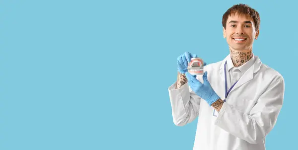 Male dentist holding jaw model on light blue background with space for text