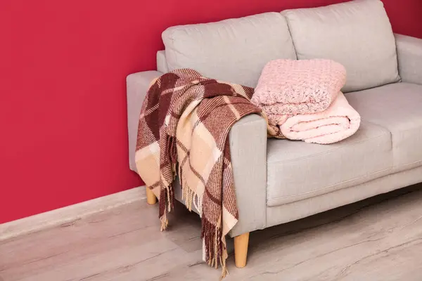 New soft blankets on sofa near burgundy wall in room
