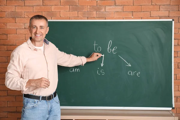 Male teacher writing English grammar on blackboard in classroom