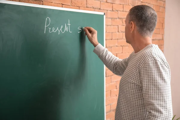 Male teacher writing English grammar in classroom